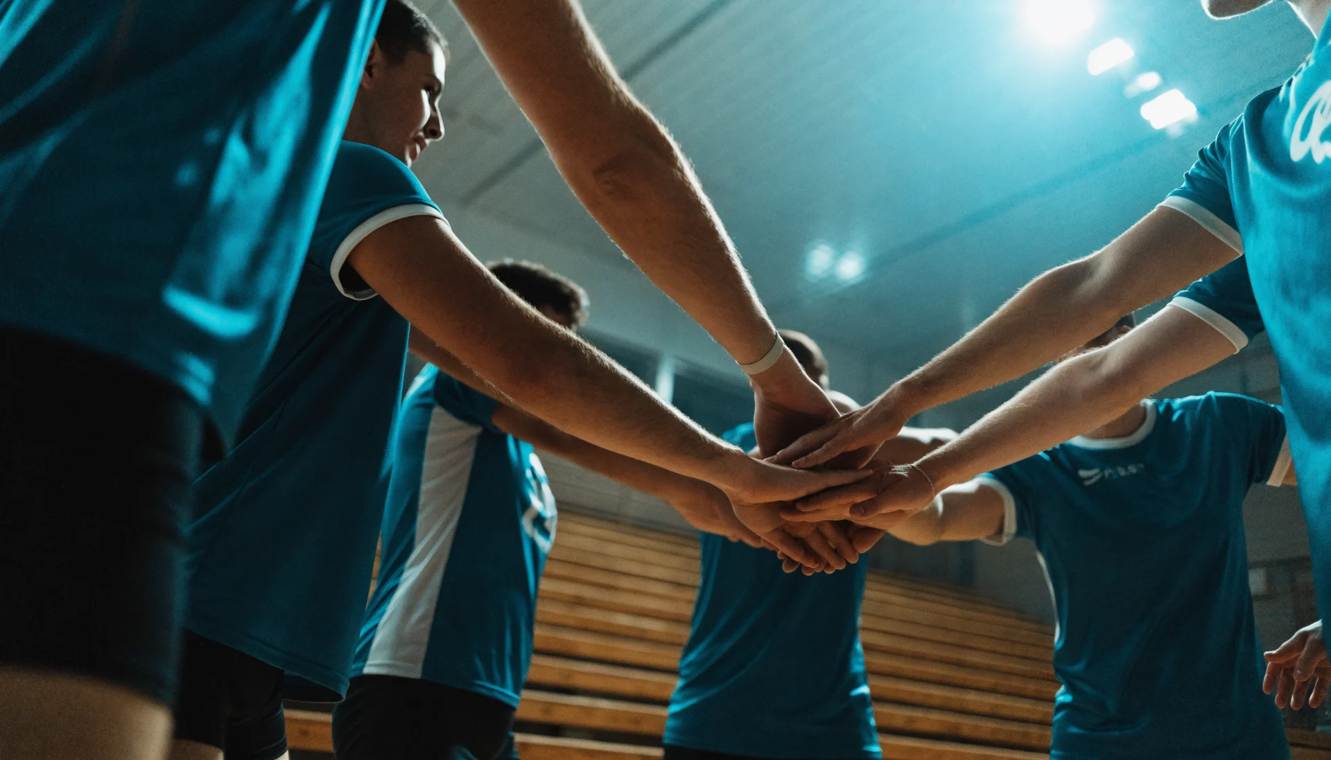 Volleyball-Mannschaft in der Halle, im Kreis mit den Händen in der Mitte, von unten fotografiert